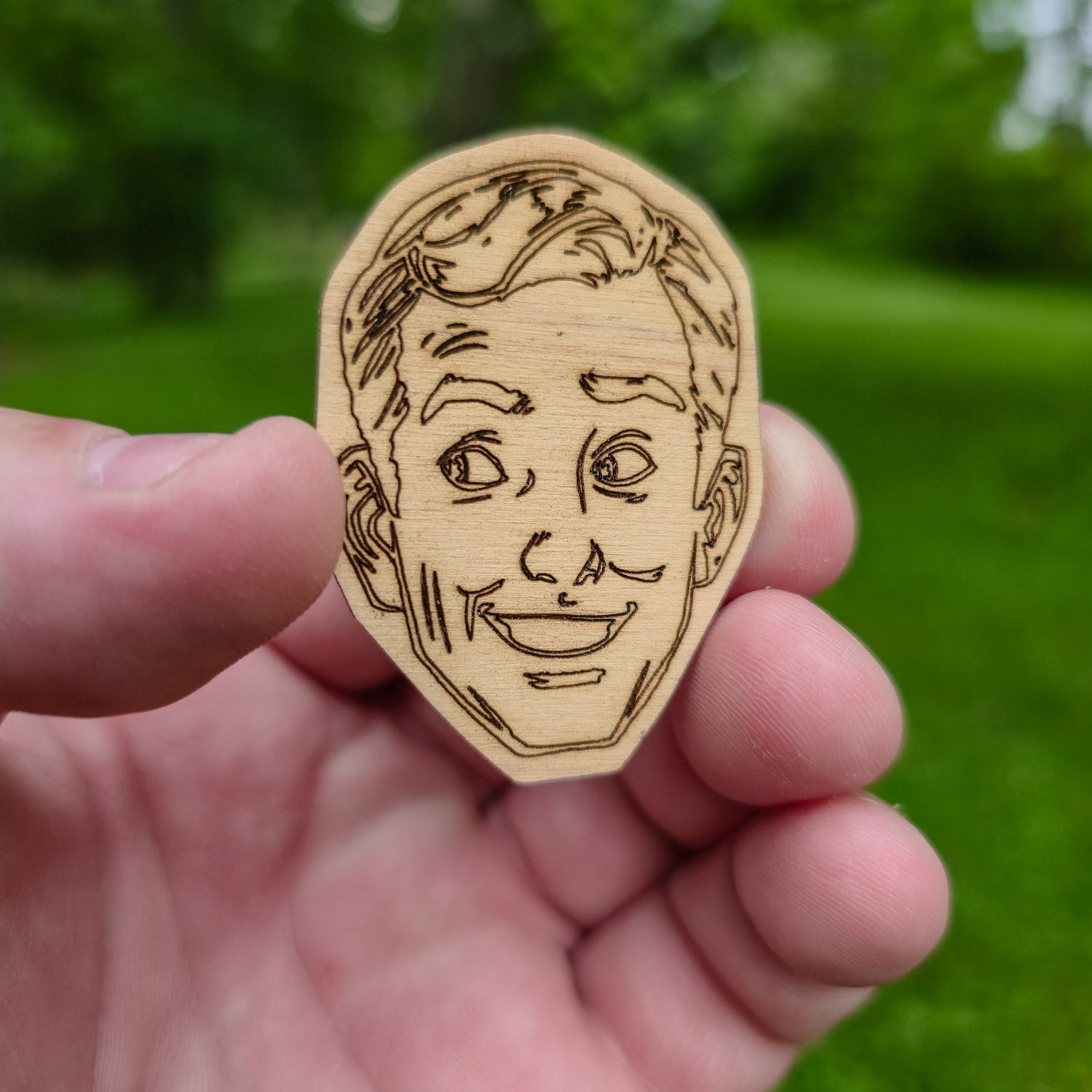 Wooden sticker with a face design held in a hand against a green background