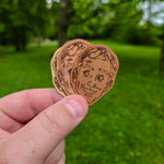 Three wooden stickers with engraved faces held against a green outdoor background