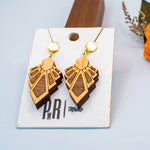 Wooden geometric earrings on a display card with flowers in the background