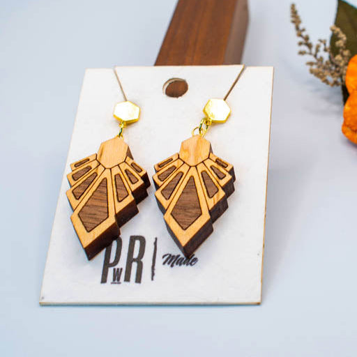 Wooden geometric earrings on a display card with flowers in the background