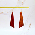 Wooden earrings hanging from a gold rod on a marble background