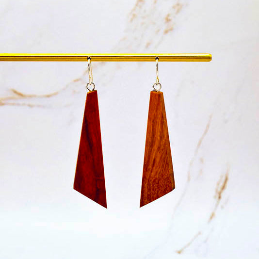 Wooden earrings hanging from a gold rod on a marble background