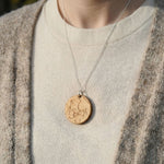 Personalized star chart necklace made from olivewood, laser-engraved, oval pendant on a silver chain, shown against cream sweater.