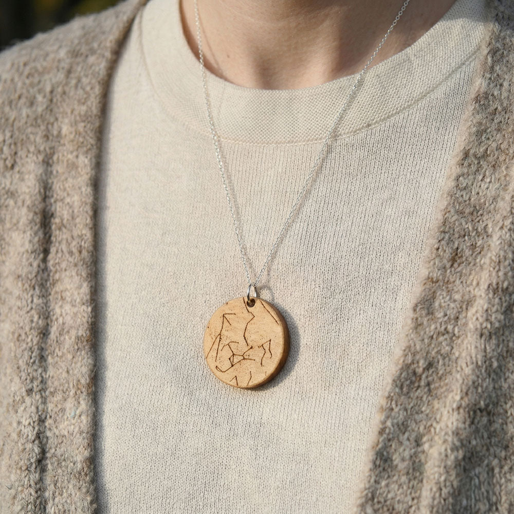 Personalized star chart necklace made from olivewood, laser-engraved, oval pendant on a silver chain, shown against cream sweater.