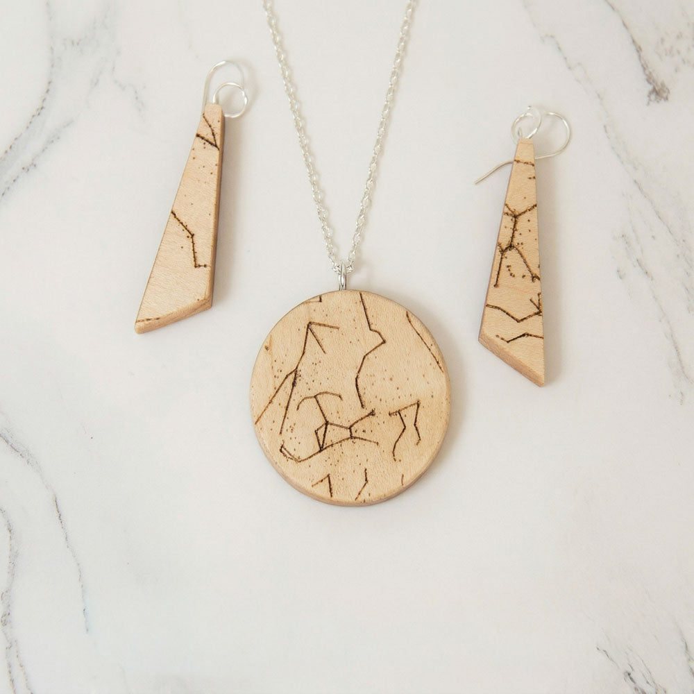 Matched set of personalized olivewood star chart jewelry, round engraved pendant on a sterling silver chain beside a pair of engraved Ascent drop earrings.