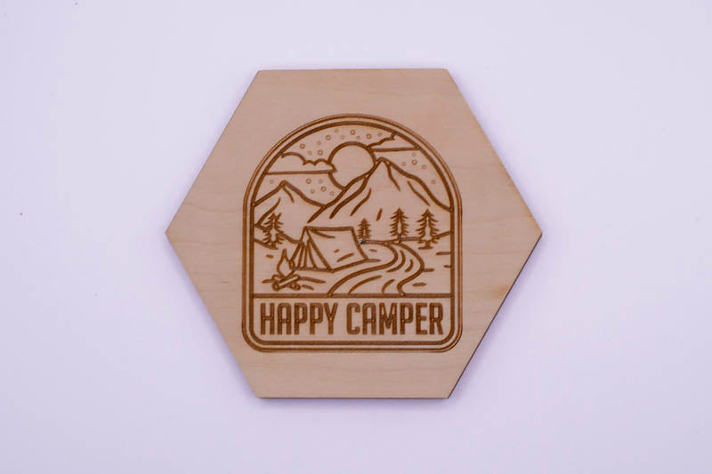 Hexagonal wooden coaster with 'Happy Camper' design on a white background