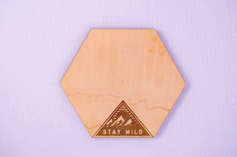 Hexagonal wooden coaster with 'Stay Wild' design on a light purple background
