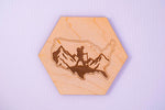 Hexagonal wooden coaster with engraved design of a person hiking in the mountains on a light purple background