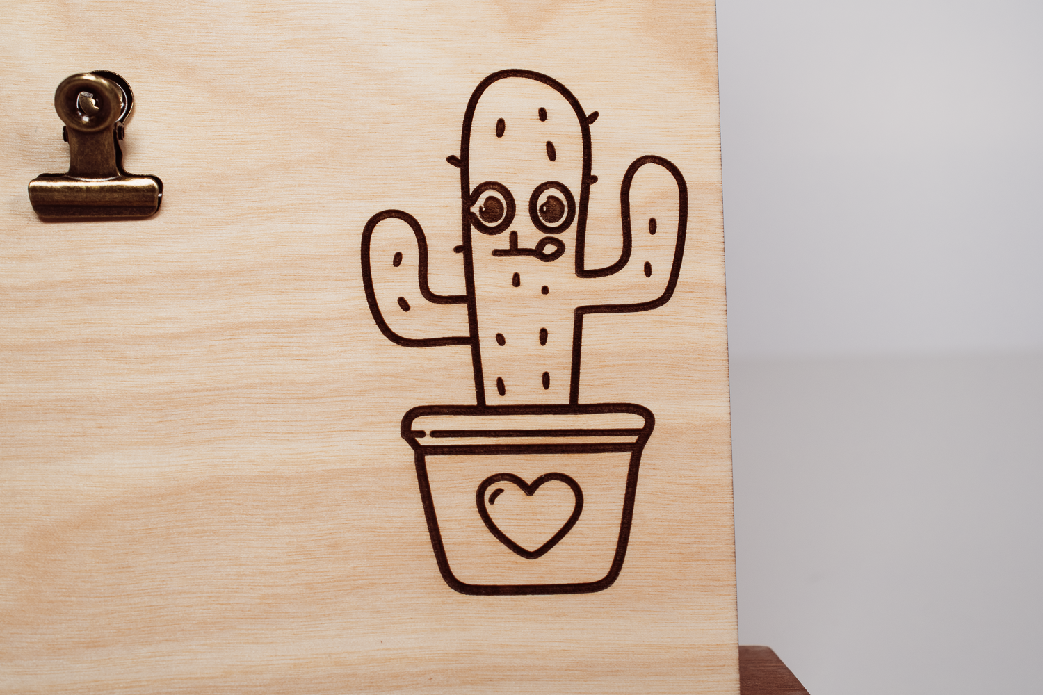Wooden message board with clip, laser-engraved with a line art cactus in a heart-shaped pot with a smiling face; light natural finish.