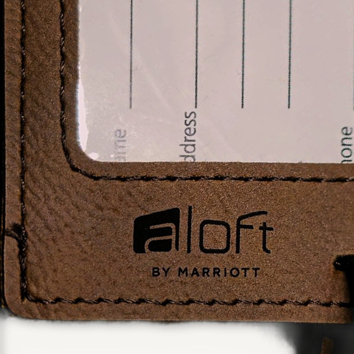 Close-up of black laser engraving on a dark brown leatherette luggage tag, showing the stitched edge