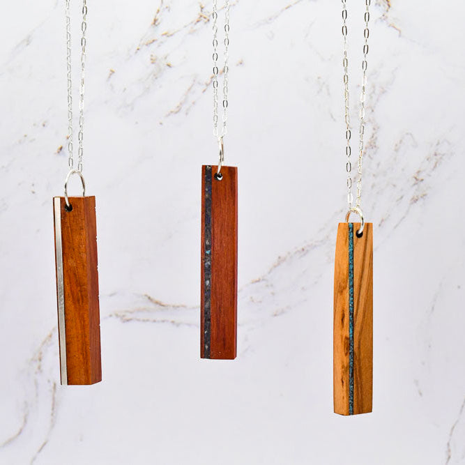 Three wooden pendant necklaces hanging against a marble background