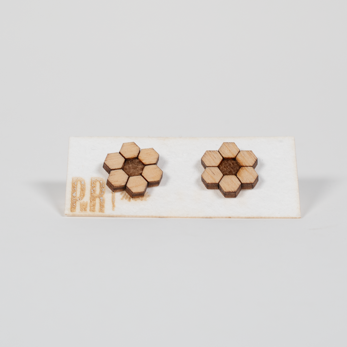 Hive wood stud earrings with laser-engraved honeycomb pattern, natural wood finish on white card with gold PRW Made branding.