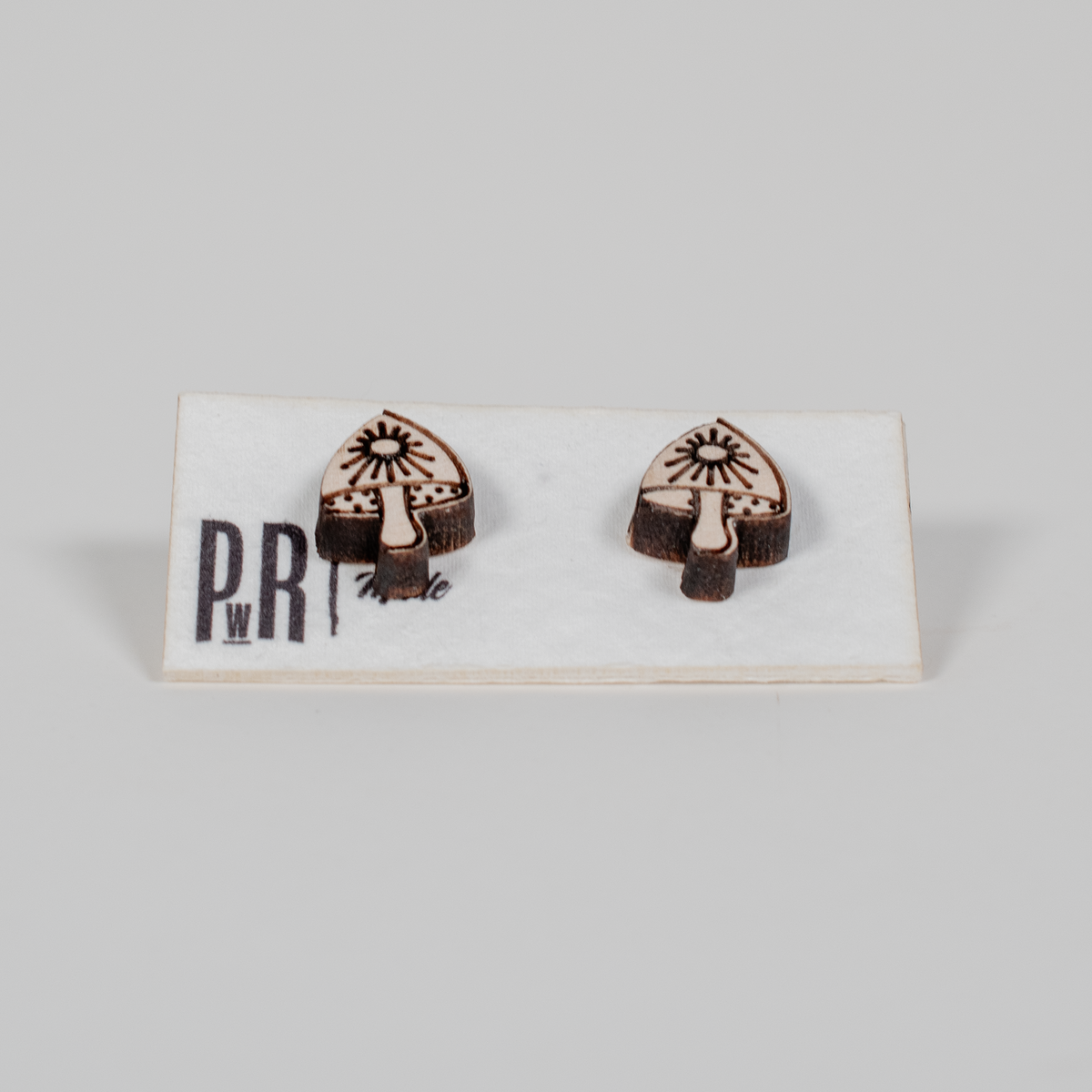 Handcrafted mushroom-shaped wooden stud earrings with black geometric laser engraving, displayed on a branded PRW Made card.
