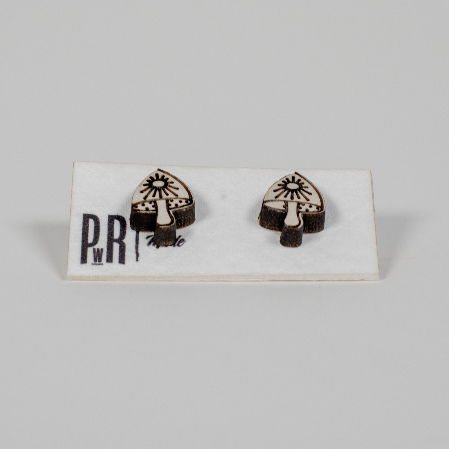 Handcrafted mushroom-shaped wooden stud earrings with black geometric laser engraving, displayed on a branded PRW Made card.