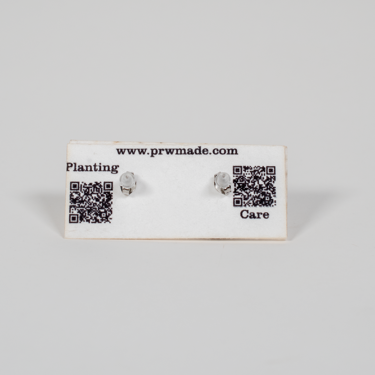 Pair of small handcrafted wooden stud earrings featuring geometric laser-engraved designs, displayed on branded care card.