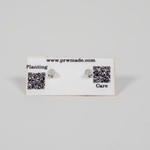 Pair of small handcrafted wooden stud earrings featuring geometric laser-engraved designs, displayed on branded care card.