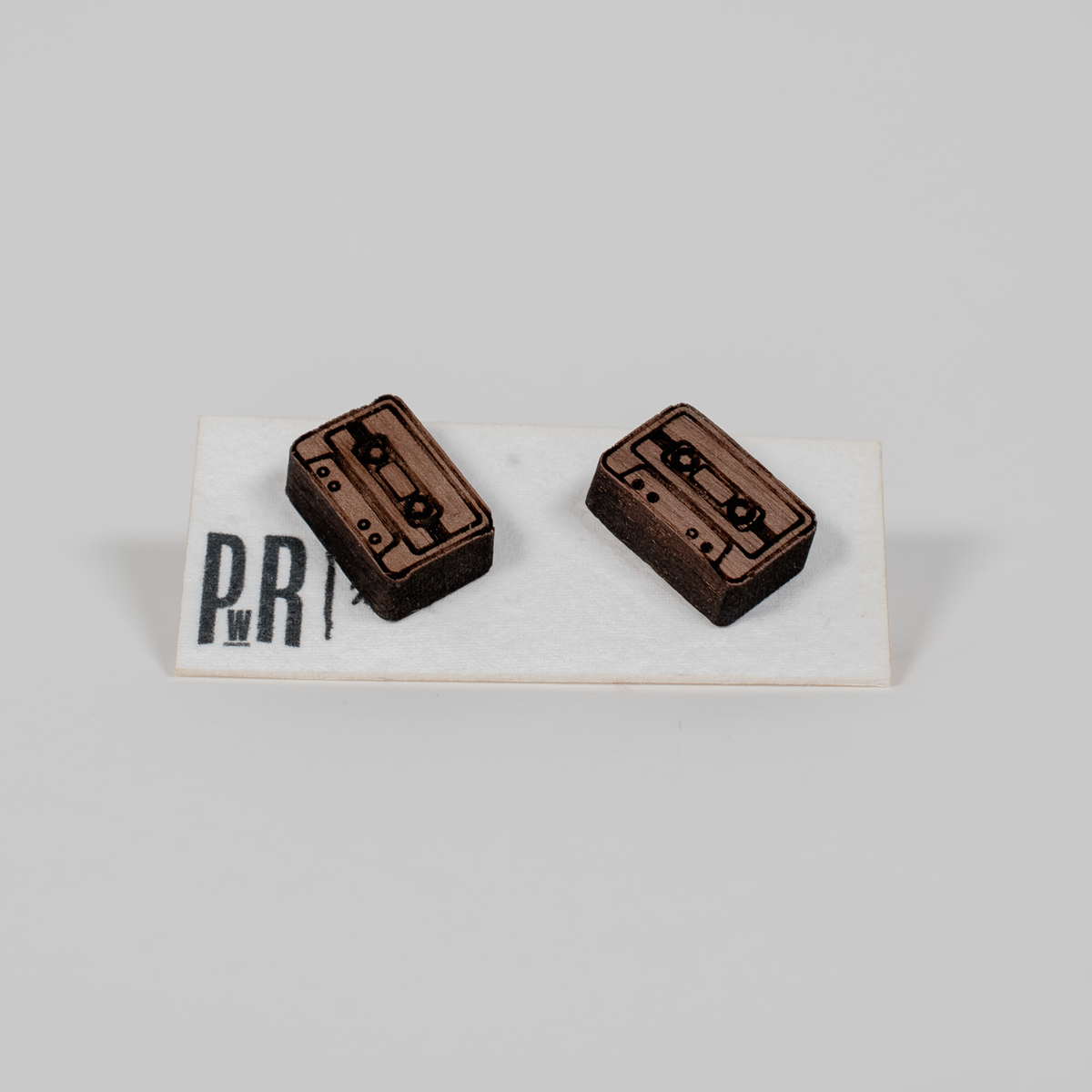 Pair of small laser-engraved wood stud earrings with geometric cassette tape design, natural finish, displayed on branded card.