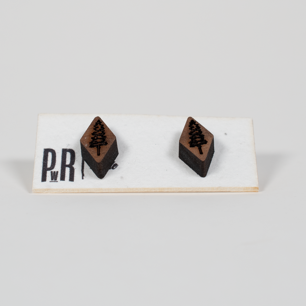 Pair of handcrafted walnut stud earrings with geometric laser-engraved designs, displayed on a white card. Dark brown wood finish.
