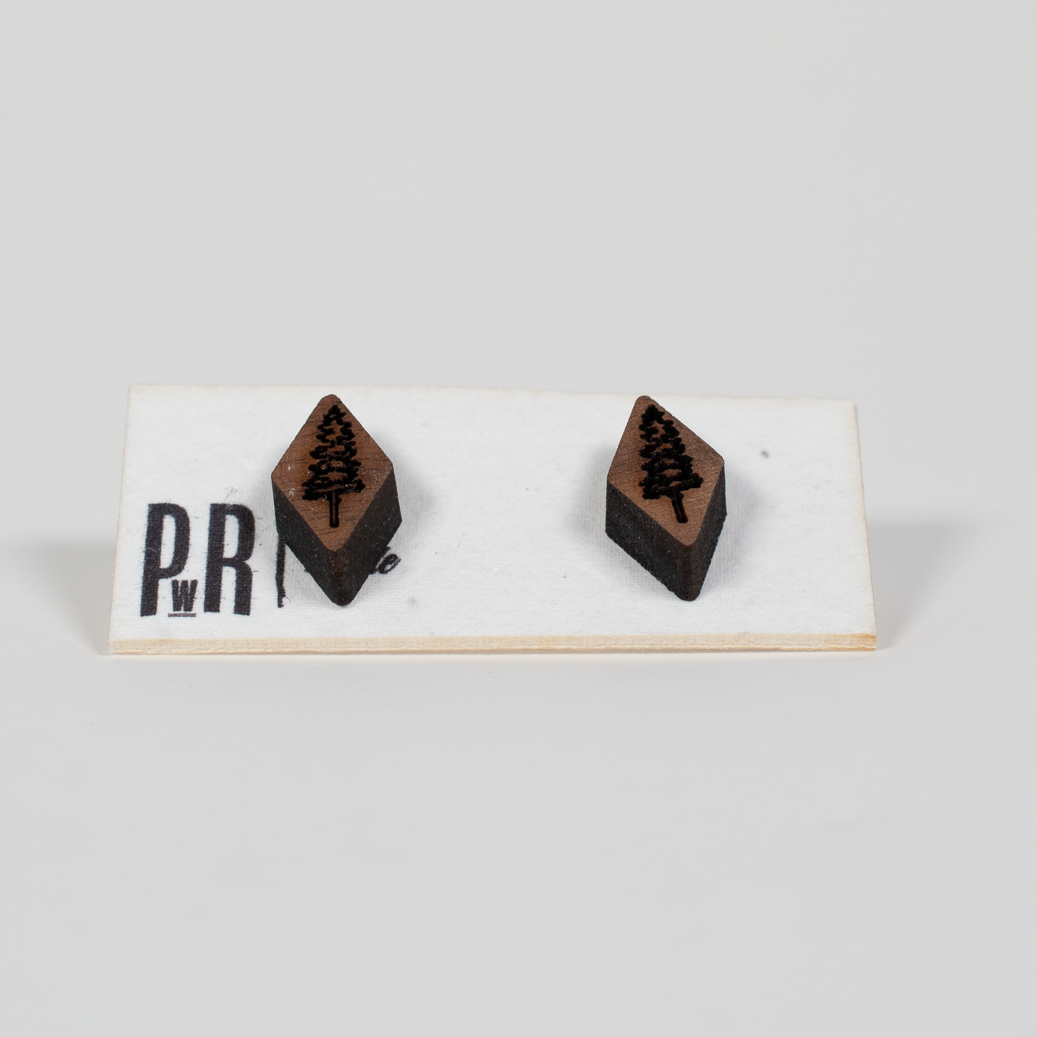 Pair of handcrafted walnut stud earrings with geometric laser-engraved designs, displayed on a white card. Dark brown wood finish.