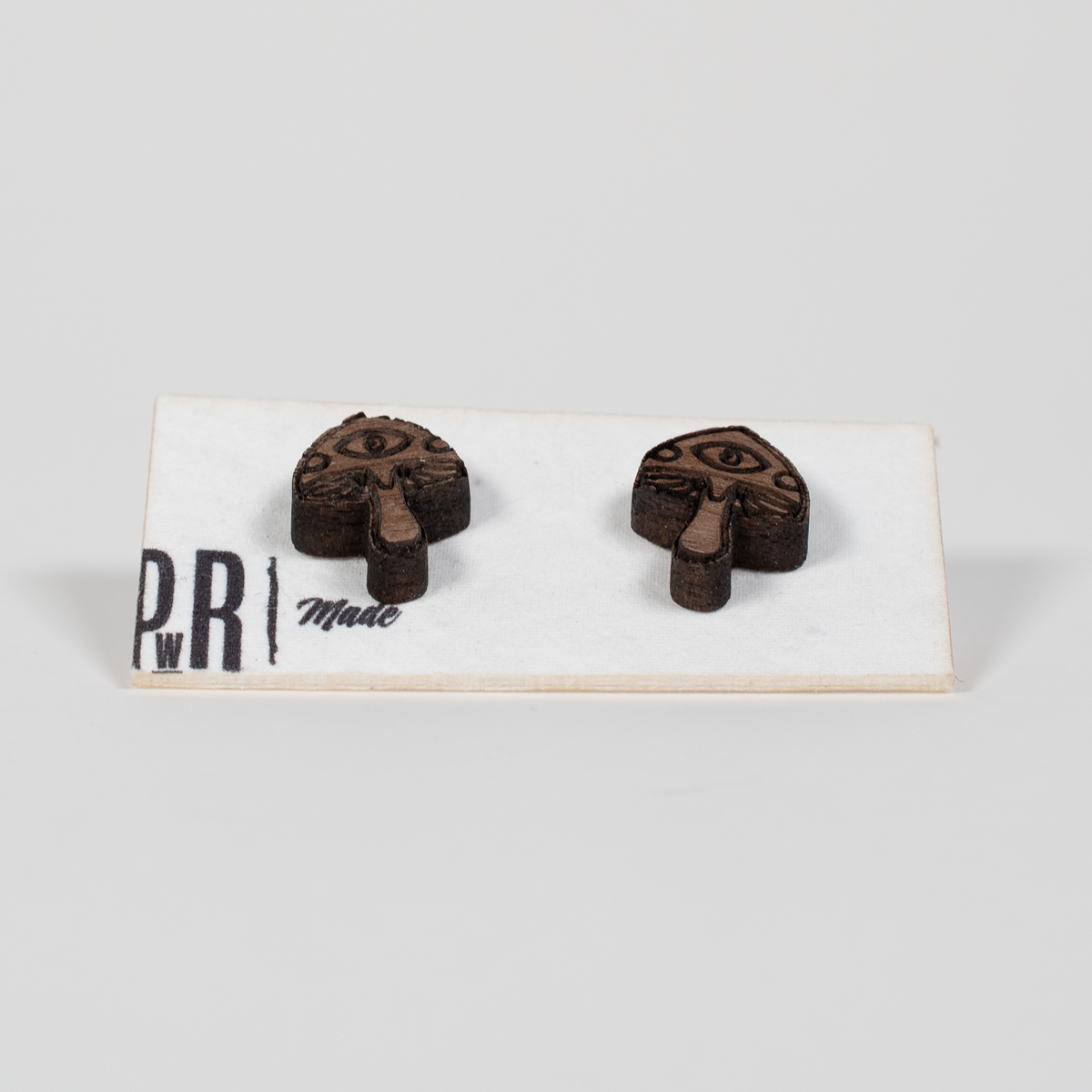 Walnut wood stud earrings, mushroom-shaped with engraved eye detail, geometric design. Hypoallergenic posts, displayed on card.