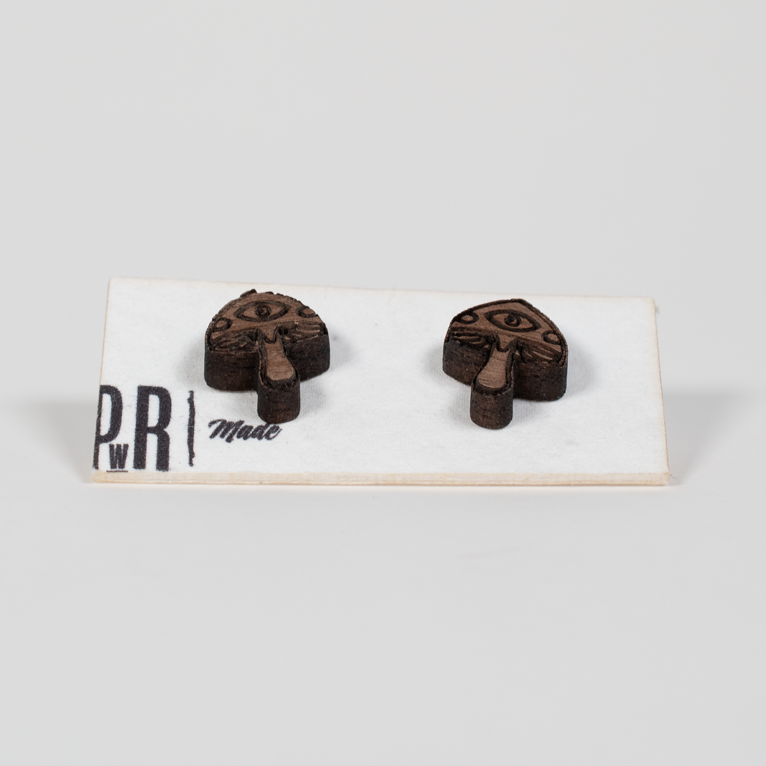 Walnut wood stud earrings, mushroom-shaped with engraved eye detail, geometric design. Hypoallergenic posts, displayed on card.