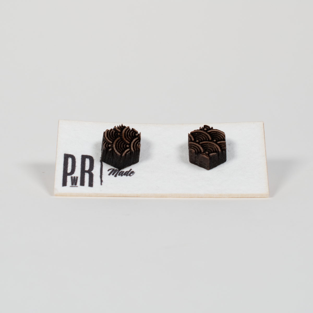 Pair of handcrafted walnut wood stud earrings with laser-engraved geometric designs on white PRW Made card, natural matte finish.
