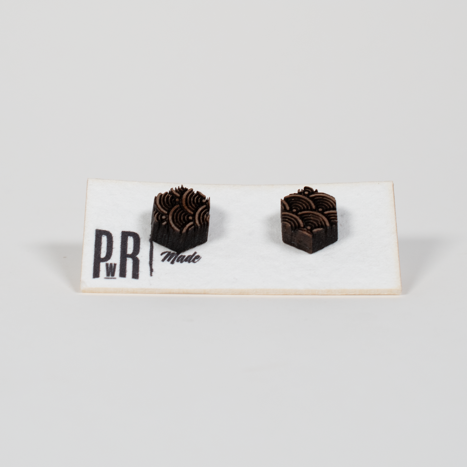 Pair of handcrafted walnut wood stud earrings with laser-engraved geometric designs on white PRW Made card, natural matte finish.