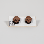 Small wooden skull stud earrings with geometric engraved design, natural wood finish, displayed on a branded PRW Made white card.