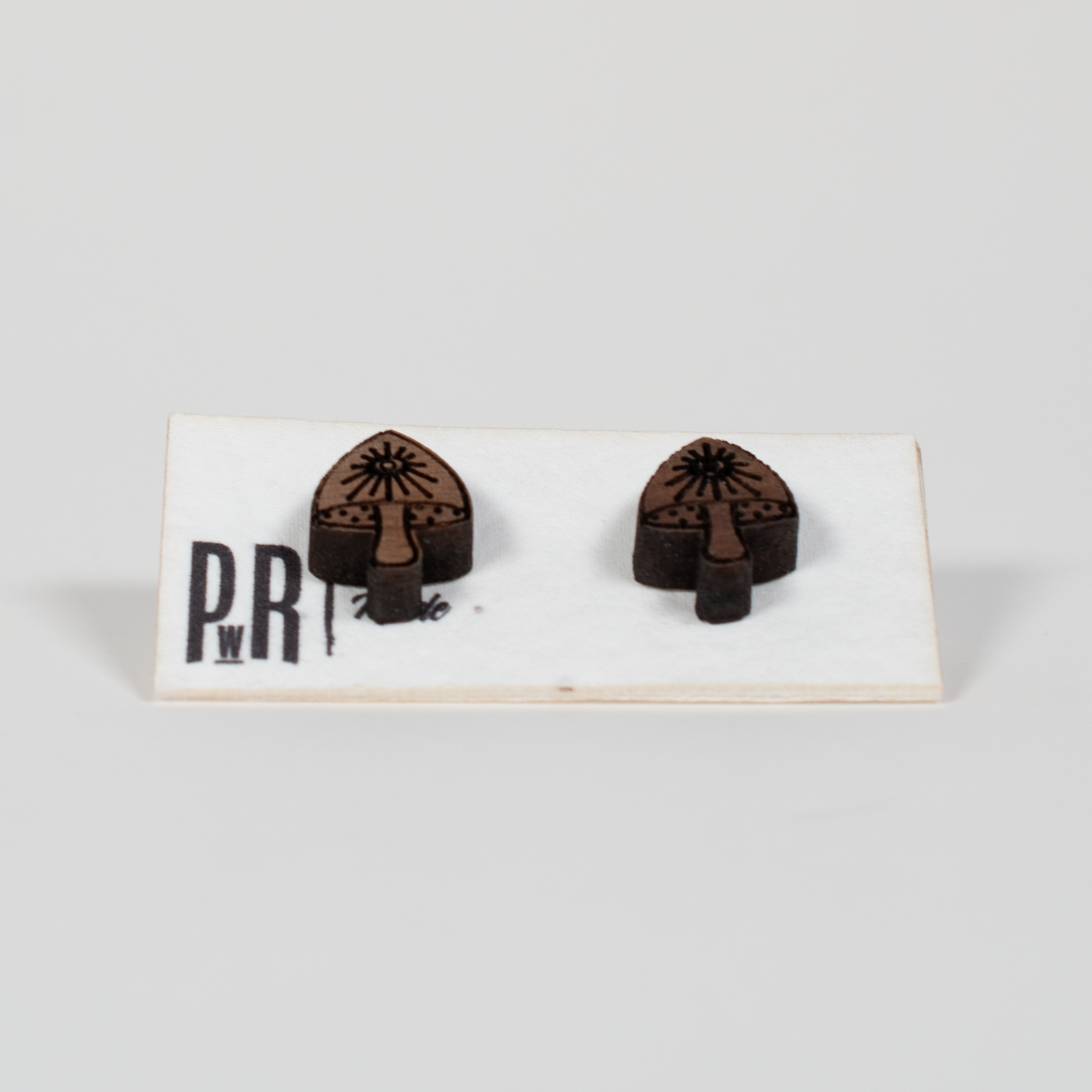 Handcrafted walnut wood stud earrings with engraved geometric designs, displayed on a white card. Hypoallergenic posts.