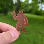 Hand holding a brown sticker cutout of a big foot against a green outdoor background