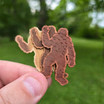 Wooden bear-shaped sticker held in a hand with a blurred green outdoor background