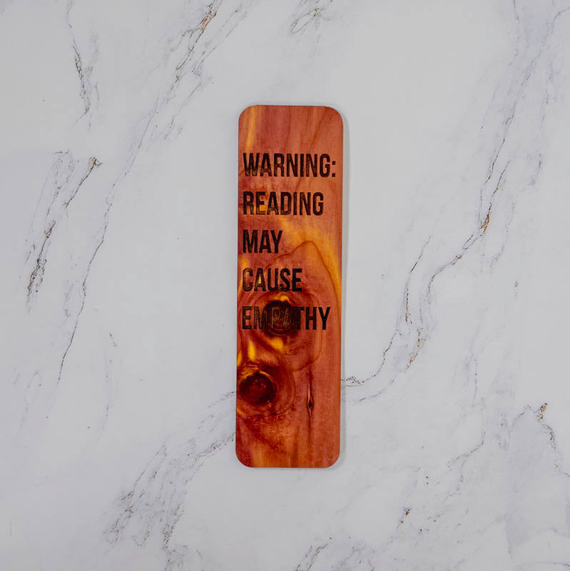 Aromatic cedar bookmark with Warning: Reading May Cause Empathy in bold lettering, knotty red grain, by PRWMade