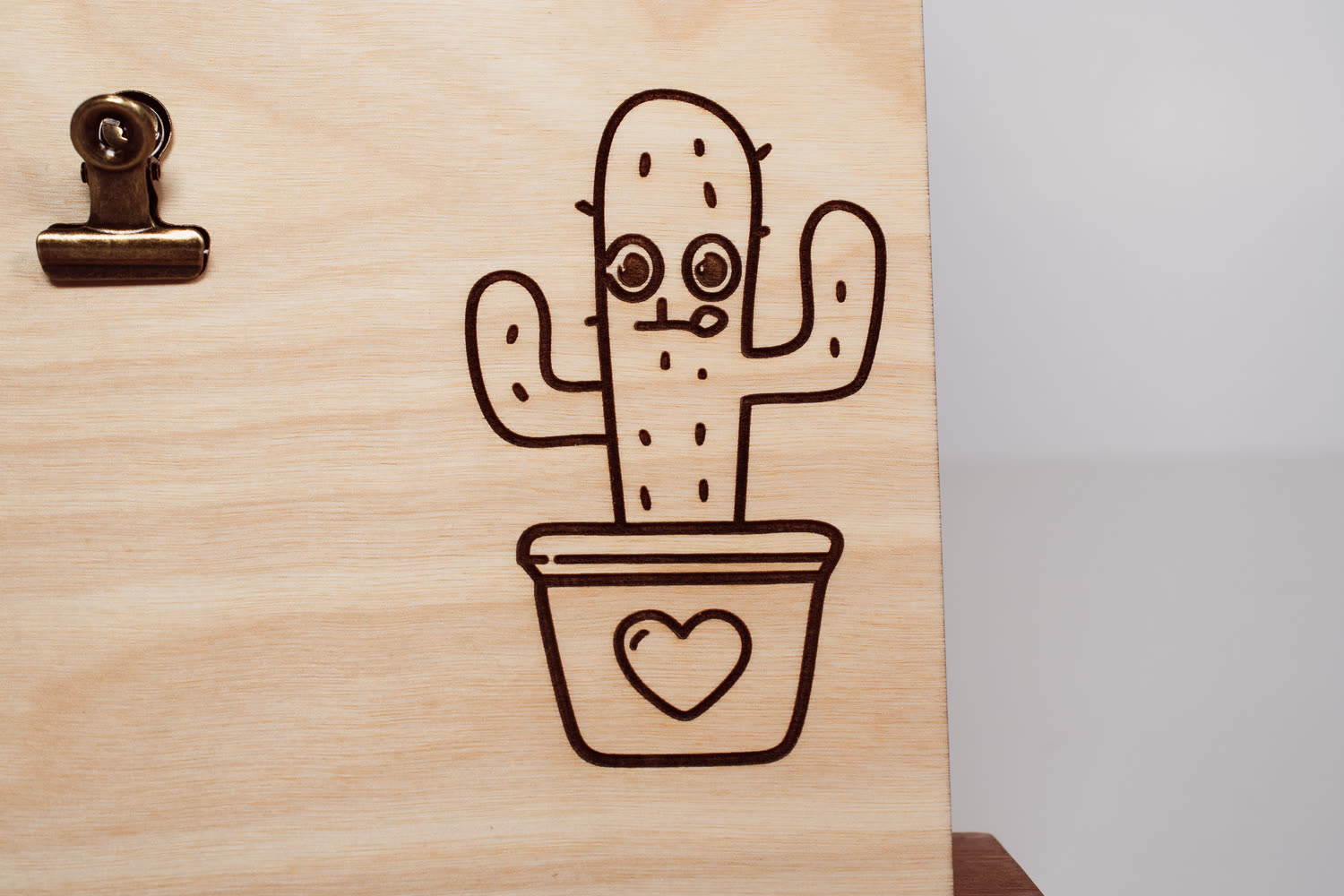 Detail of a line art cactus in a heart-shaped pot laser engraved on a light natural wood message board by PRWMade
