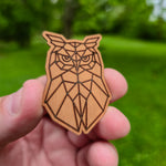Wooden owl-shaped sticker held in a hand with a green blurred background