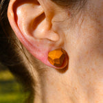 Close-up of an ear wearing a geometric orange earring with a blurred natural background