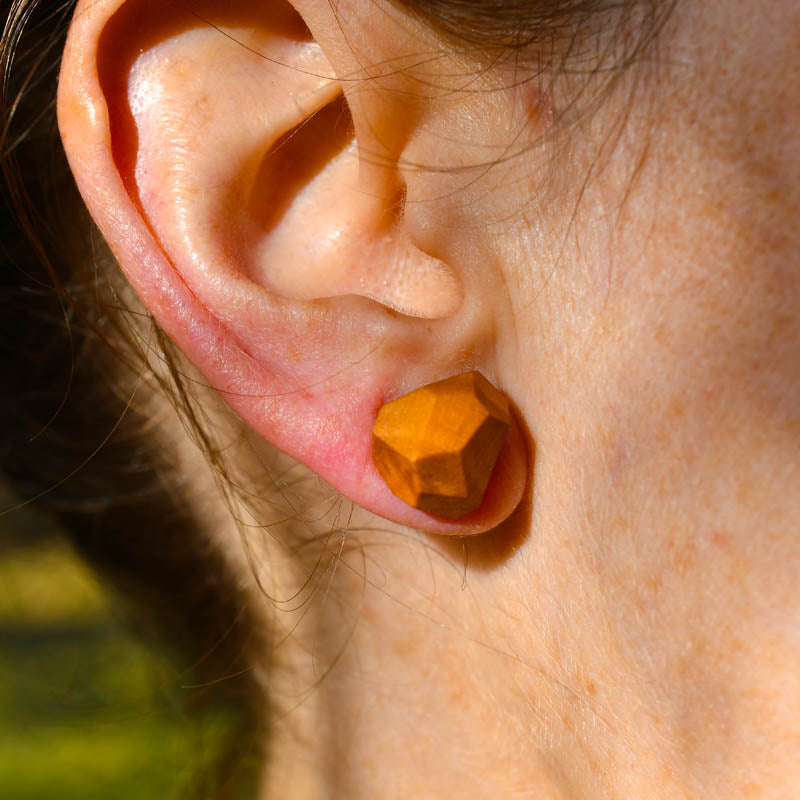Close-up of an ear wearing a geometric orange earring with a blurred natural background