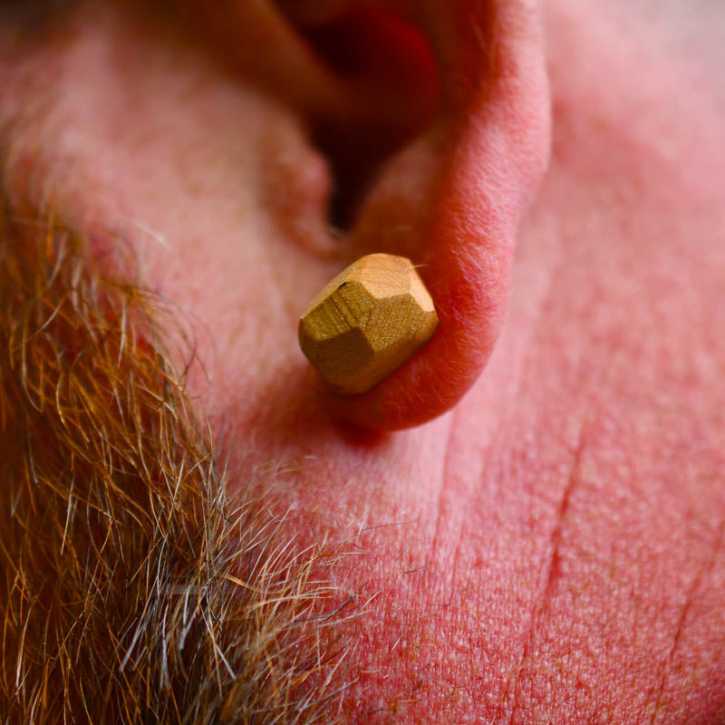 Wooden earbud in a person's ear with a close-up view of the ear and beard.