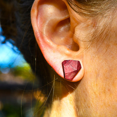 Close-up of an ear wearing a red geometric earring with a blurred natural background