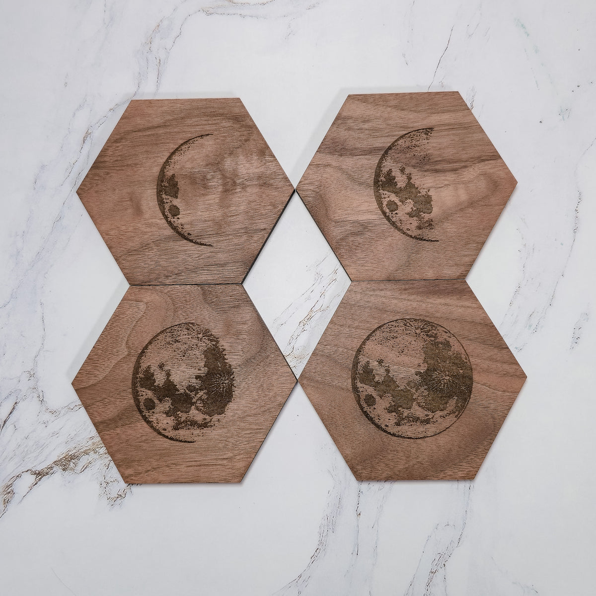 Four walnut moon phase coasters in a 2x2 flat lay on marble, crescents and full moons