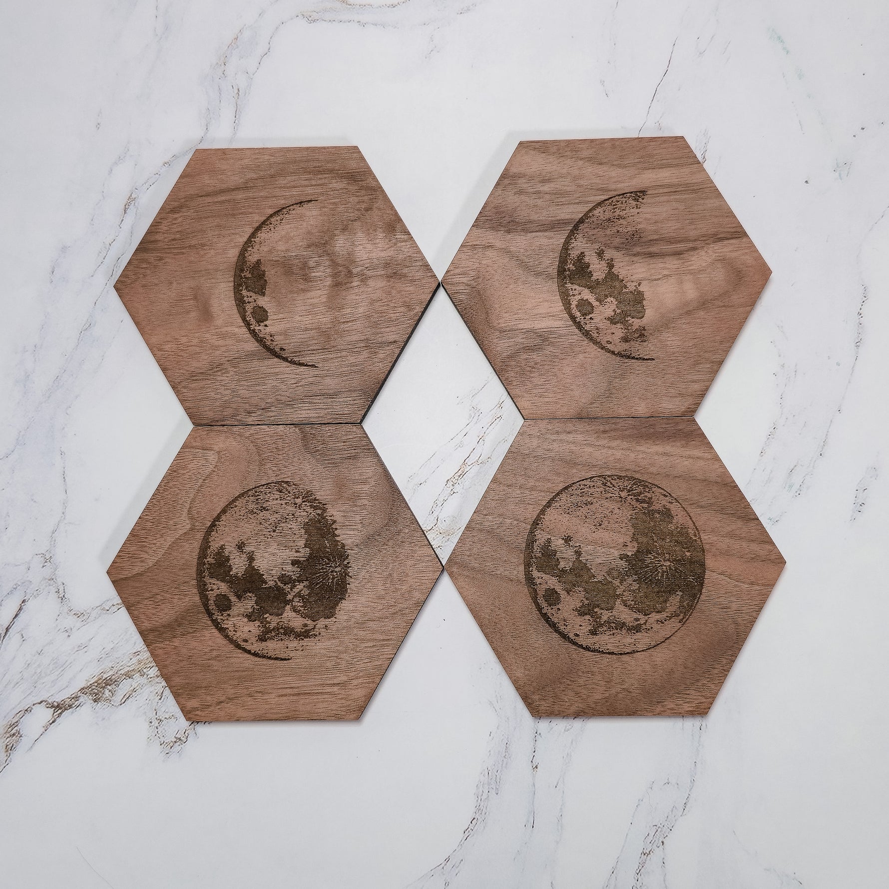 Four walnut moon phase coasters in a 2x2 flat lay on marble, crescents and full moons