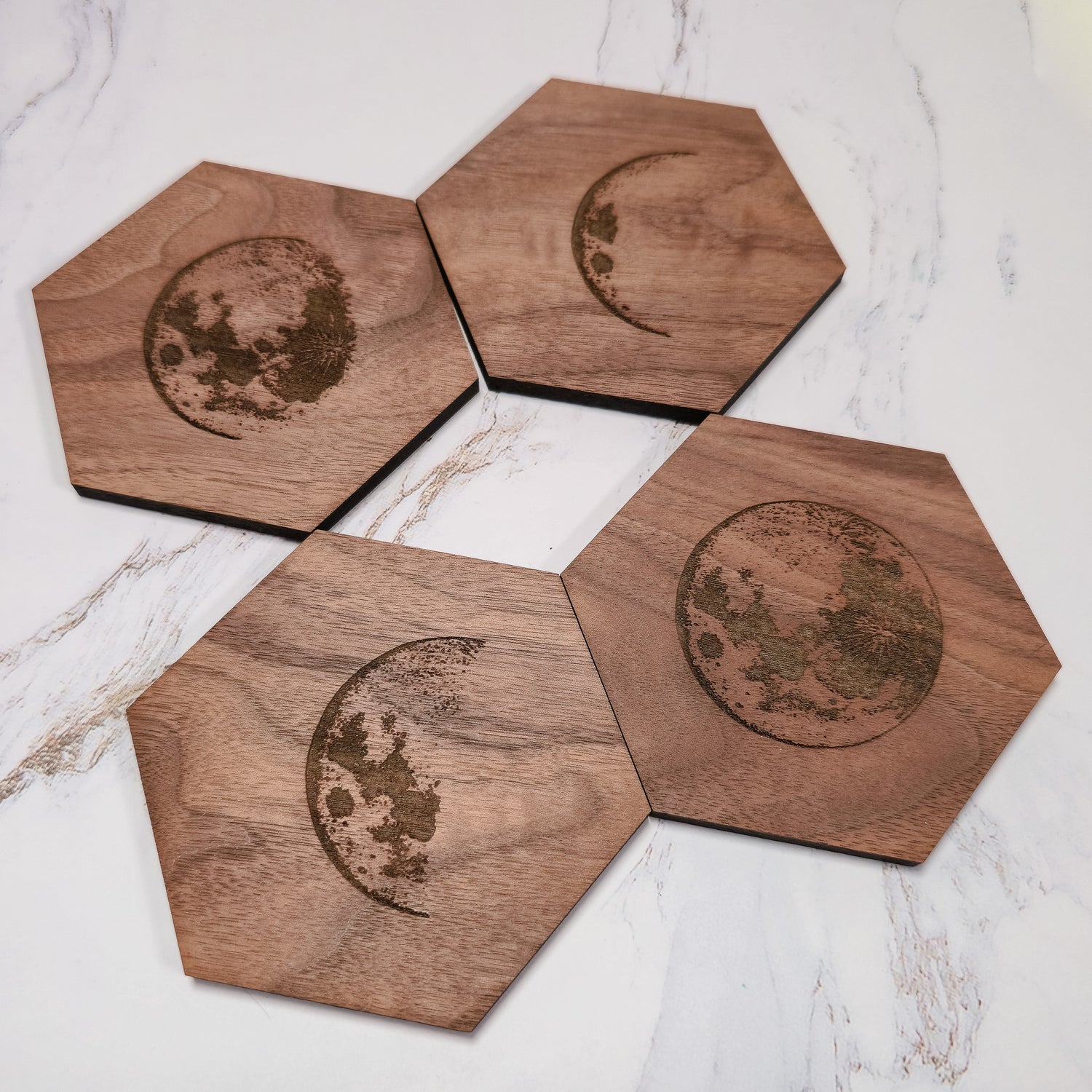 Set of four walnut hexagon moon phase coasters arranged on white marble, lunar cycle laser engraving