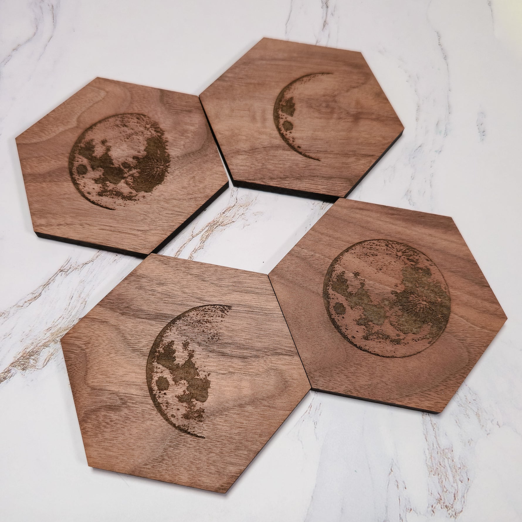 Set of four walnut hexagon moon phase coasters arranged on white marble, lunar cycle laser engraving