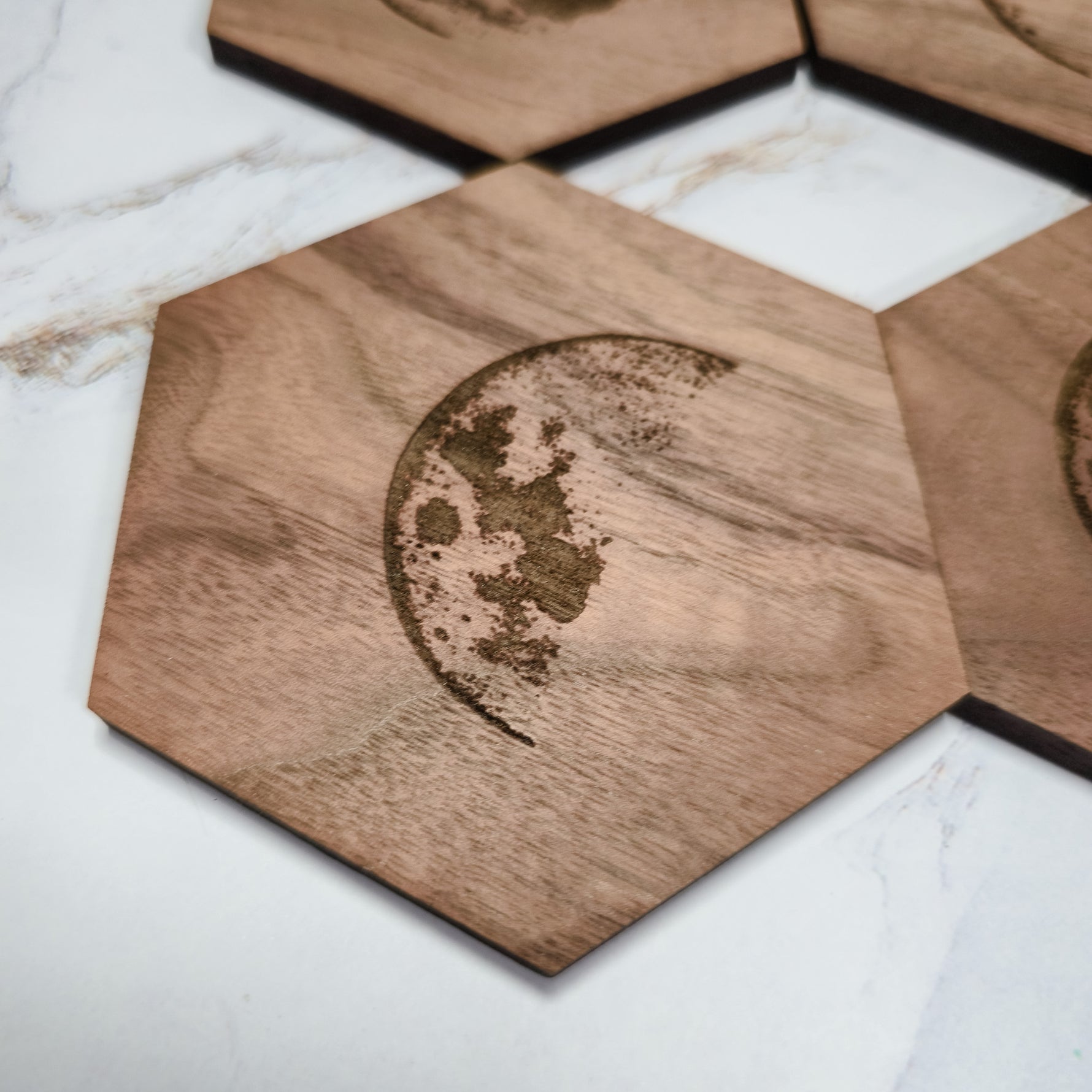 Close-up of a walnut hexagon coaster with detailed waxing crescent moon laser engraving
