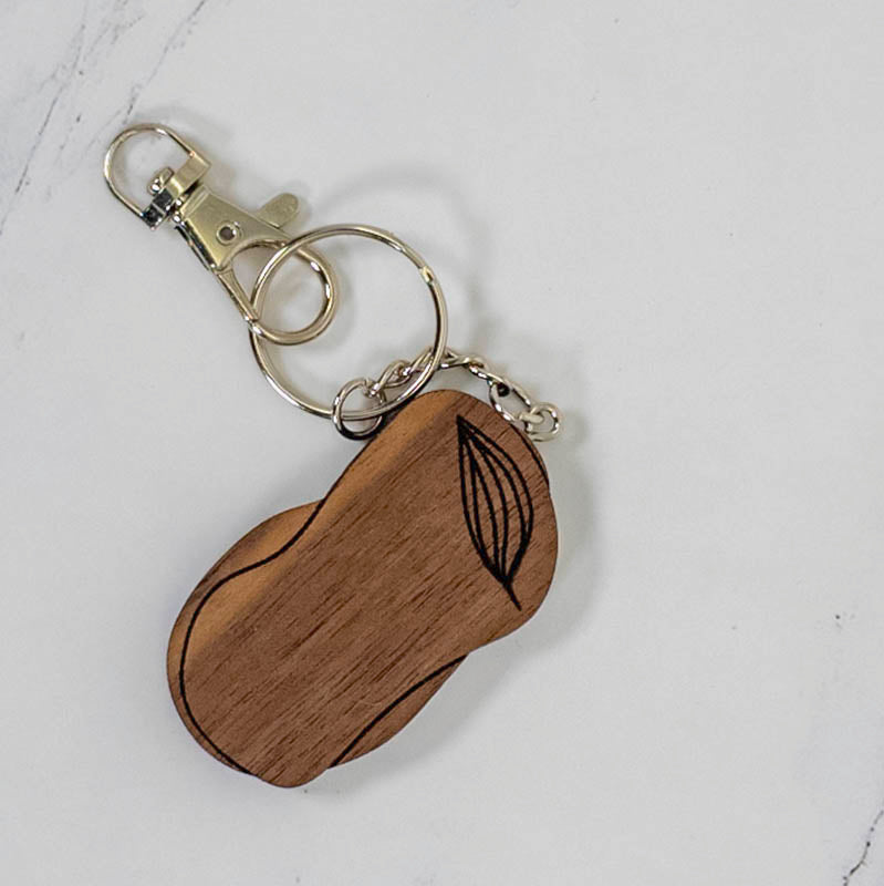 Large organic pebble-shaped walnut wood keychain engraved with a botanical leaf line drawing, dark grain and silver hardware, by PRWMade