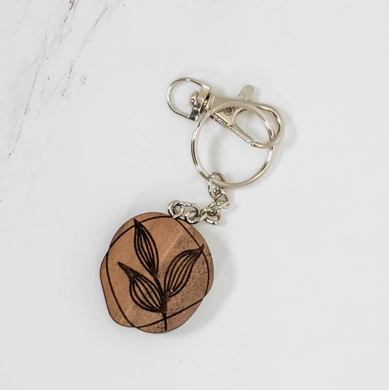 Small round walnut wood keychain engraved with a botanical leaf line drawing, dark grain with silver hardware, by PRWMade