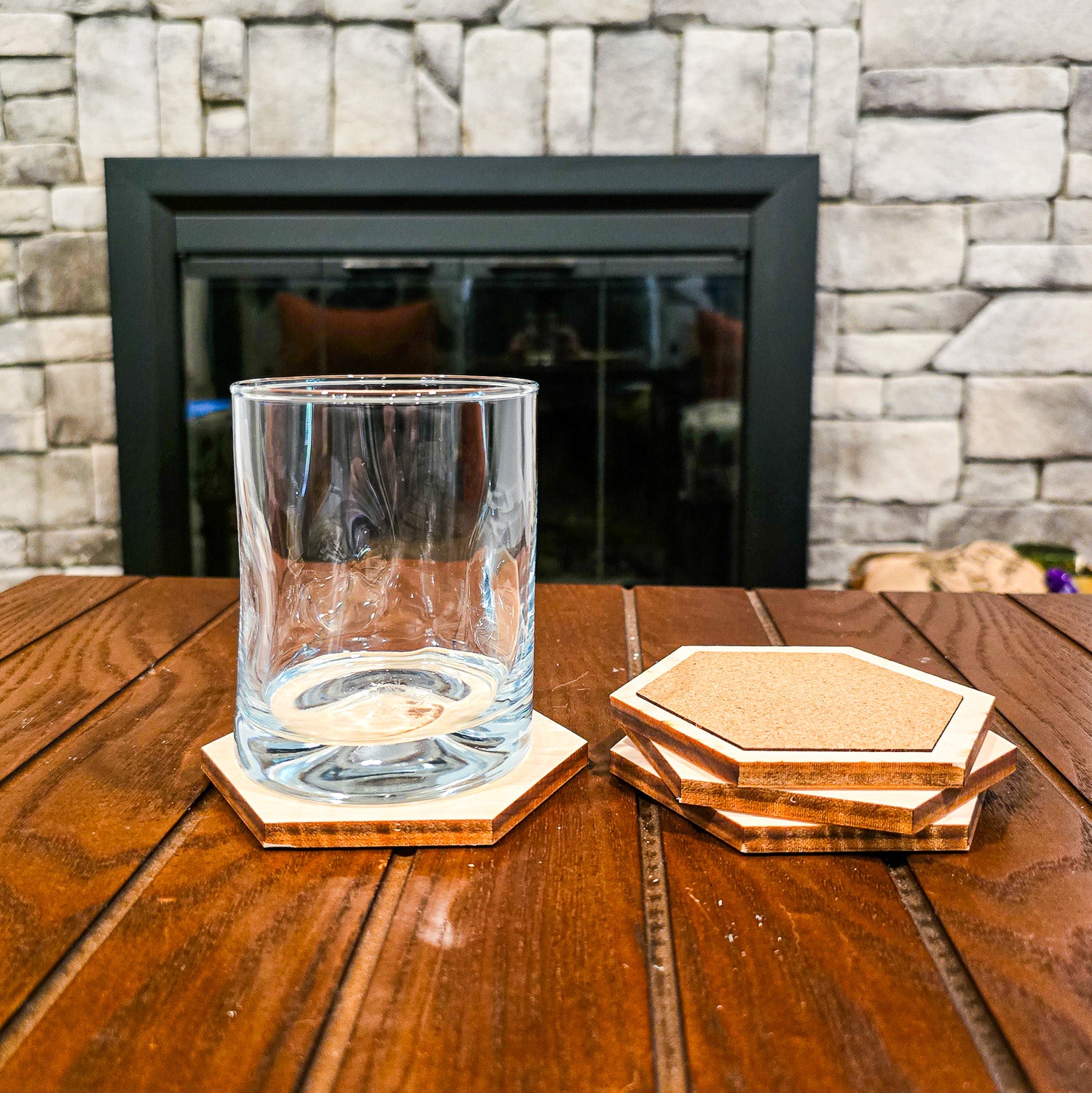 Clear glass on a wooden table with wooden hexagonal coasters in front of a stone fireplace.