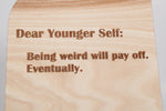 Close-up of the engraved lettering on the Dear Younger Self wooden message board, showing engraved wood grain detail