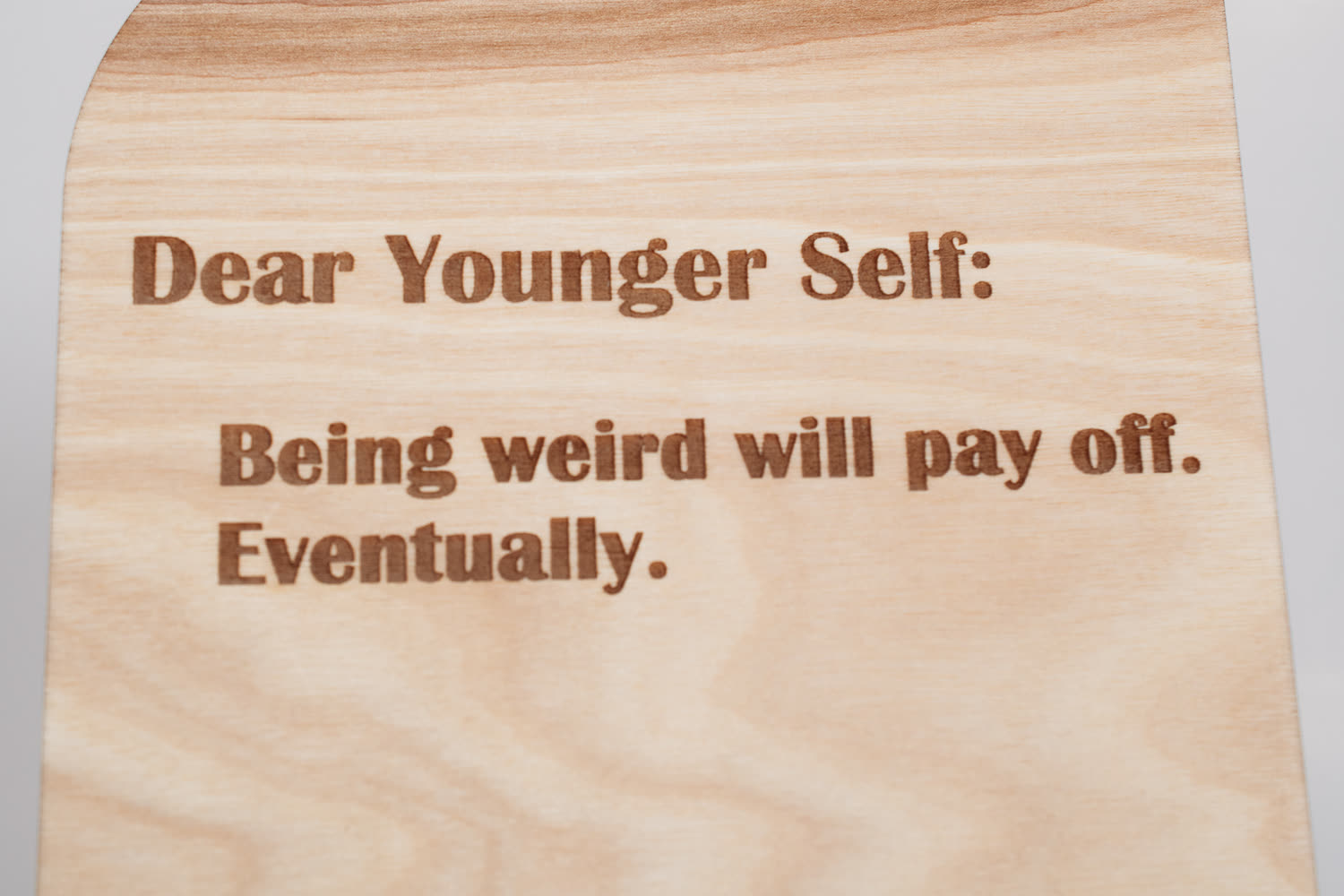 Close-up of the engraved lettering on the Dear Younger Self wooden message board, showing engraved wood grain detail